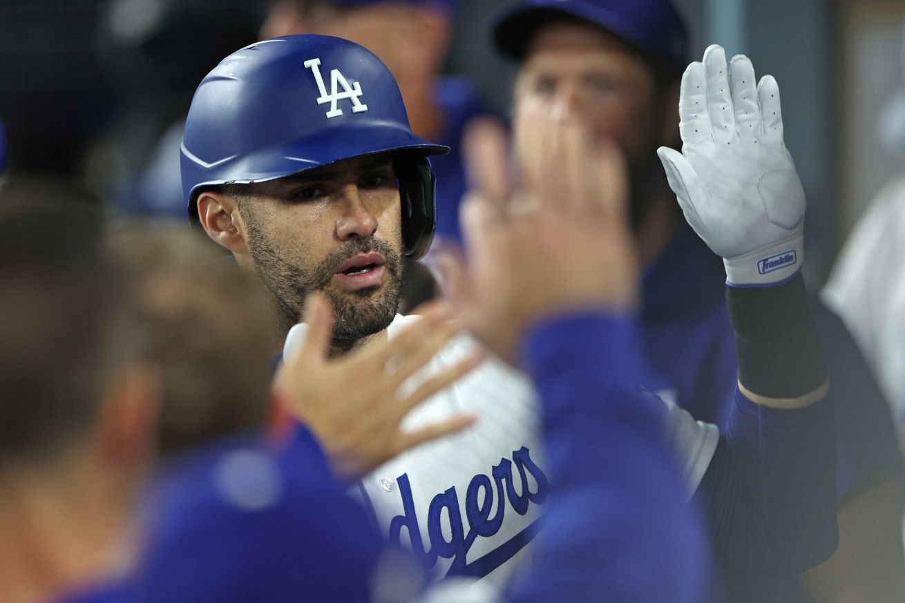 J.D. Martinez high fives teammates in a white Dodgers uniform with blue lettering and a blue helmet.