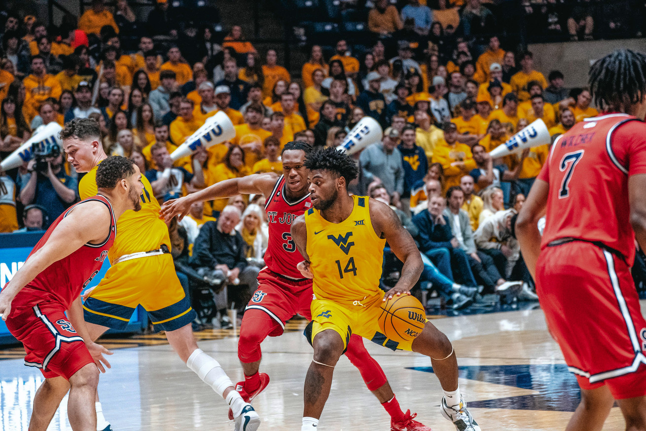 West Virginia Mountaineers basketball player Seth Wilson (#14) dribbles a basketball in front of St. John’s Red Storm basketball player Jordan Dingle (#3) during a game at WVU Coliseum in Morgantown, West Virginia on December 1, 2023 