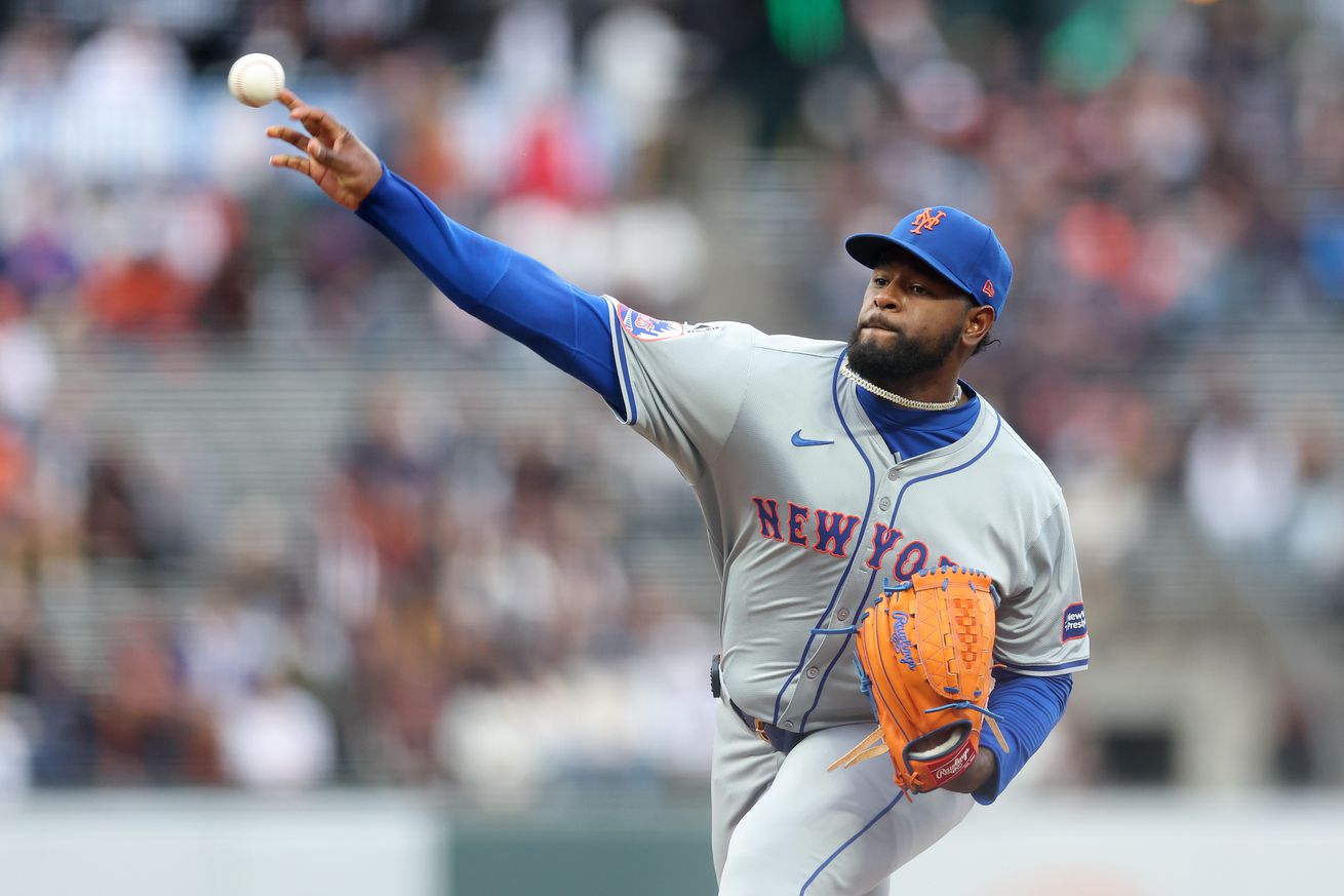 Luis Severino throws a pitch in a grey road Mets jersey with blue lettering, orange outlines, and a blue hat with an orange Mets logo on the front.