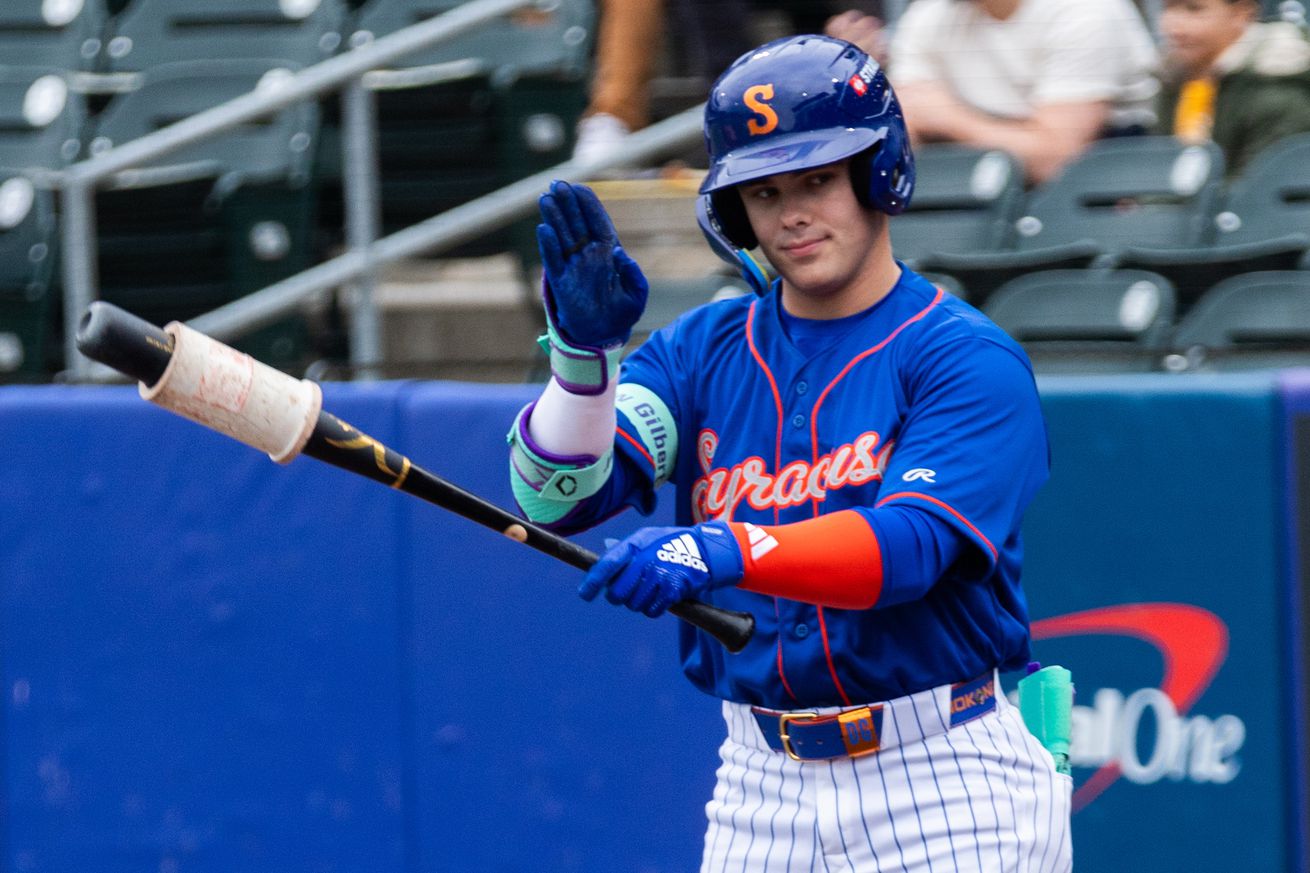 Drew Gilbert waves as he holds a bat in the on-deck circle while wearing a blue Syracuse Mets jersey with white pants with pinstripes.