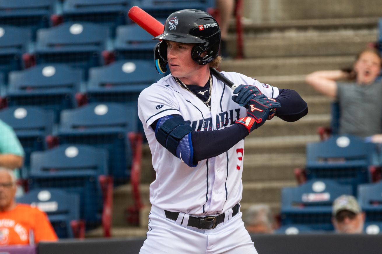 Ryan Clifford stands in the batter’s box in a white Rumble Ponies uniform with a dark blue helmet and sleeves and a red bat.